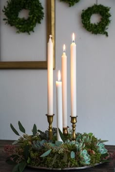 four candles are lit on a table with greenery