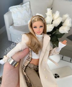 a barbie doll sitting on top of a table next to a vase with white flowers