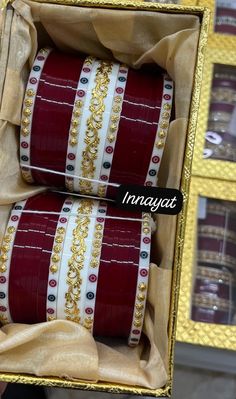 two red and white bracelets are in a box with gold trimming on them