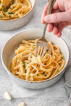 someone is holding a fork over a bowl of pasta with parmesan cheese and garlic