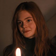 a young woman holding a lit candle in her right hand and looking at the camera