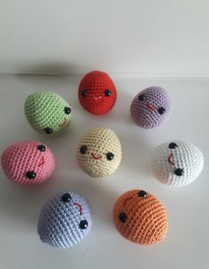 six crocheted balls with faces are arranged in a circle on a white surface