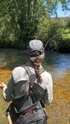 a woman standing in shallow water holding onto a fishing rod with her back to the camera