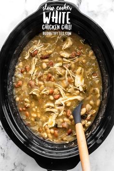 slow cooker white chicken chili in a black crock pot with a wooden spoon