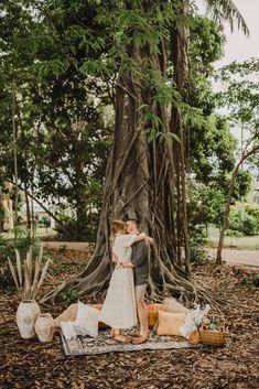 a man and woman standing in front of a tree with their arms around each other