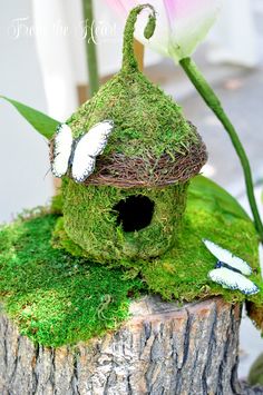 a bird house made out of moss on top of a tree stump with flowers in the background