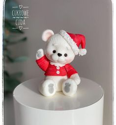 a small white teddy bear sitting on top of a white cake plate wearing a santa hat and red sweater