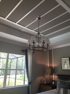 a chandelier hangs from the ceiling above a bed in a room with gray walls