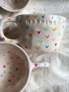 two cups with spoons sitting next to each other on a white tablecloth covered surface