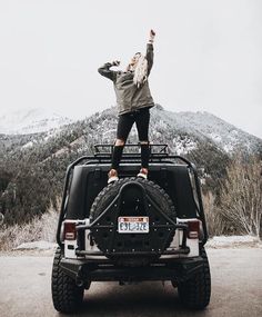 a woman standing on the back of a black four - doored vehicle with her arms in the air