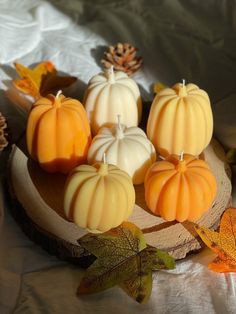 small pumpkin candles sitting on top of a wooden plate next to leaves and pine cones