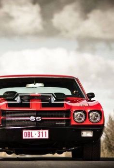 a red and black muscle car parked on the side of the road with dark clouds in the background