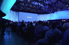 people are sitting on chairs in front of a stage with the facebook logo projected on it