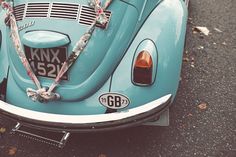 an old blue vw bug parked on the side of the road with ribbons tied to it