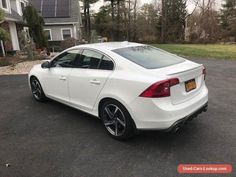 a white car parked in a parking lot next to a house with trees behind it