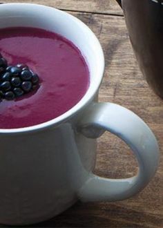 a close up of a cup of soup with berries on the top and another bowl in the background