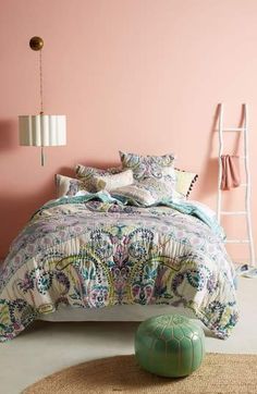 a bedroom with pink walls and a bed covered in a colorful comforter, along with a green footstool