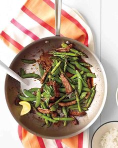 a pan filled with green beans and meat on top of a red and white towel