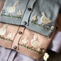 two sweaters with ducks on them are sitting next to a flower and some daisies