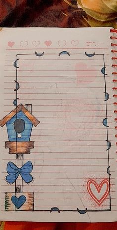 an open notebook with a birdhouse drawn on it and a flower in the background