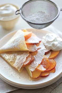 a white plate topped with slices of fruit covered in powdered sugar and whipped cream