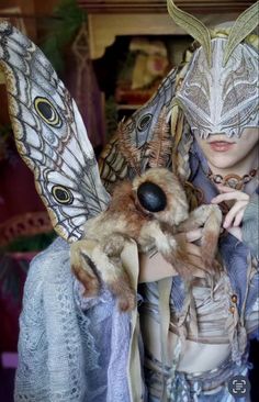 a woman with an animal mask on her face and wings over her head, holding a teddy bear