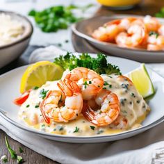 shrimp and broccoli covered in white sauce on a plate with lemon wedges