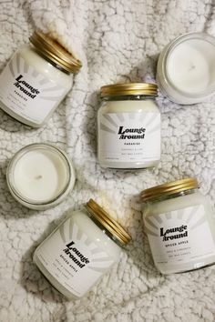 four jars of candles sitting on top of a white blanket next to eachother