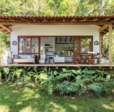 an outdoor living area in the middle of some trees and grass with lots of plants around it