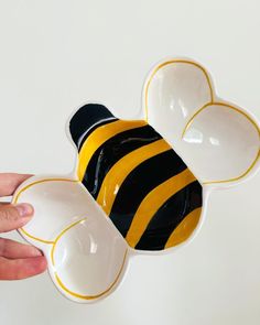 a hand holding a bee shaped bowl in front of a white wall with a black and yellow stripe on it