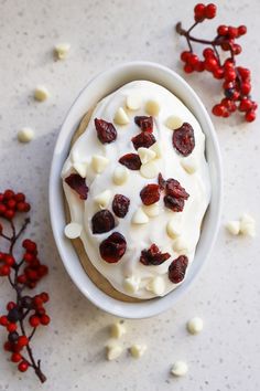 a bowl filled with white frosting and red berries on top of a table next to some leaves