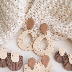 three pairs of wooden earrings sitting on top of a white surface next to a knitted blanket