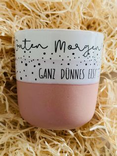 a pink and white coffee cup sitting on top of some straw covered ground with the words g