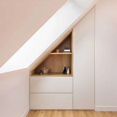 an attic bedroom with white walls and wooden flooring, built - in shelving