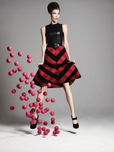 a woman in a black and red dress is surrounded by pink balls on a gray background