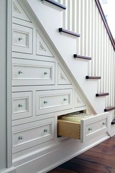 an open drawer under the stairs in a house with wood flooring and white walls