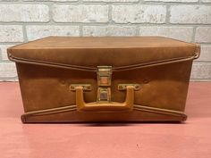 a brown suitcase sitting on top of a pink floor next to a brick wall and door