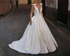 a woman in a white wedding dress standing on the side of an alleyway with buildings behind her