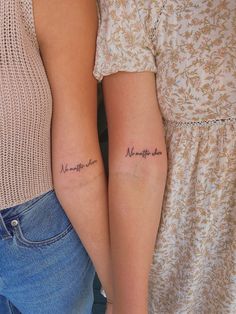 two women with matching tattoos on their arms, one is holding the other's arm