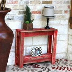 a red table sitting next to a brick wall with a lamp on top of it