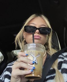 a blonde woman in sunglasses drinking from a starbucks cup while sitting in the back seat of a car