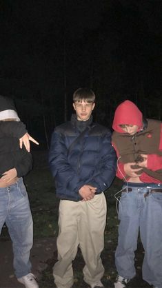 three men standing next to each other in the woods at night, one holding a cell phone