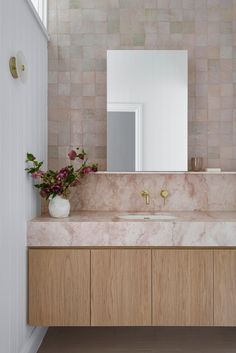 a bathroom with marble counter tops and wooden cabinets, along with a vase filled with flowers