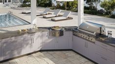 an outdoor kitchen with grill and chairs next to a swimming pool in the back yard