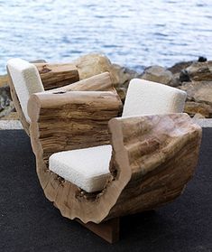 a wooden chair sitting on top of a black carpet next to the ocean and rocks