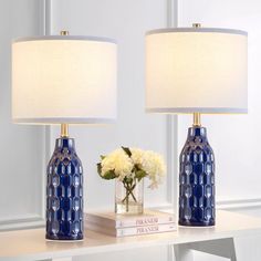 two blue vases with white flowers sit on a table next to a book and lamp