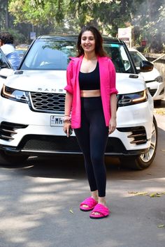 a woman standing in front of a white car wearing pink shoes and a black bra