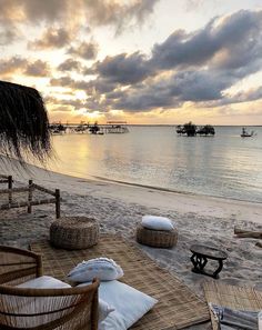 the sun is setting on an empty beach with wicker chairs and tables in front of it