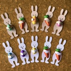 paper cut out rabbits holding carrots and an easter egg in their mouths, with other bunny decorations around them