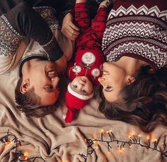 two people laying on top of a bed next to each other with christmas lights in the background